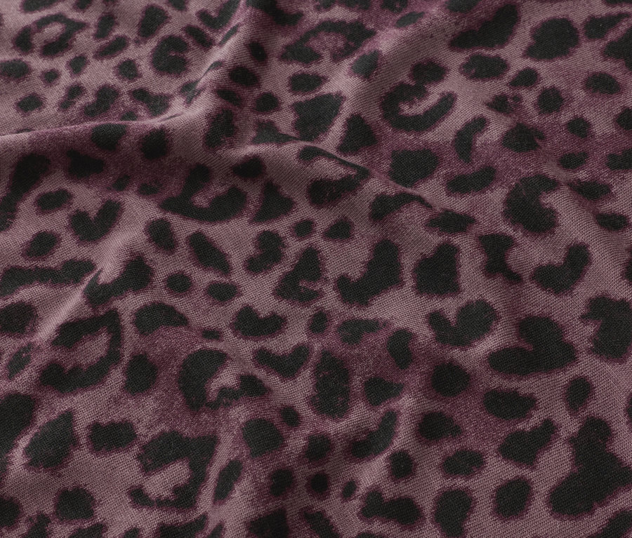 Nahaufnahme eines Stoffes mit einem schwarzen Leopardenmuster auf violettem Grund.