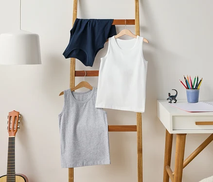 Eine Leiter hält graue, weiße und blaue Tanktops. Eine Gitarre steht neben der Leiter, und ein Schreibtisch steht daneben.