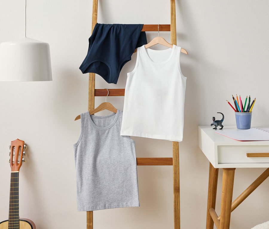 Eine Leiter hält graue, weiße und blaue Tanktops. Eine Gitarre steht neben der Leiter, und ein Schreibtisch steht daneben.