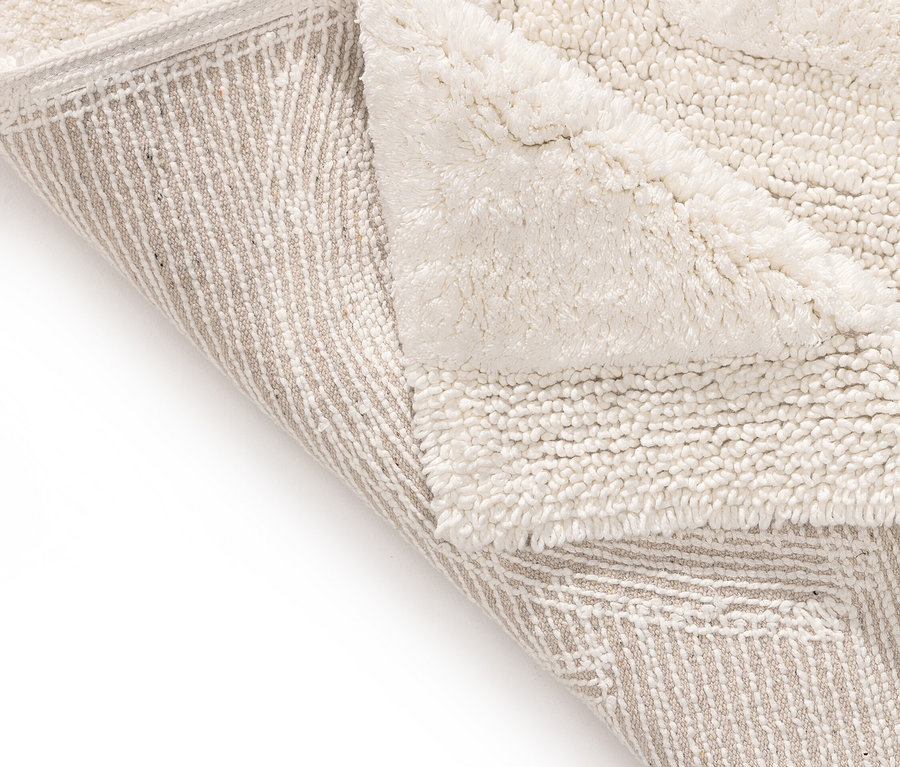 Detailansicht einer cremefarbenen Badematte, die umgeschlagen ist und eine beige Unterseite mit Streifenmuster zeigt.