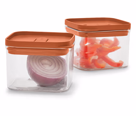Zwei durchsichtige, quadratische Behälter mit orangefarbenen Deckeln. Einer enthält eine rote Zwiebel, der andere geschnittene rote Paprika.
