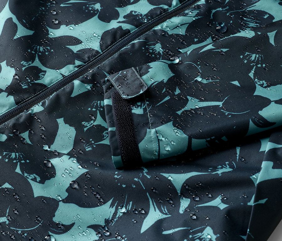 Nahaufnahme einer wasserabweisenden Jacke mit Reißverschluss und Blumenmuster, auf der Wassertropfen zu sehen sind.
