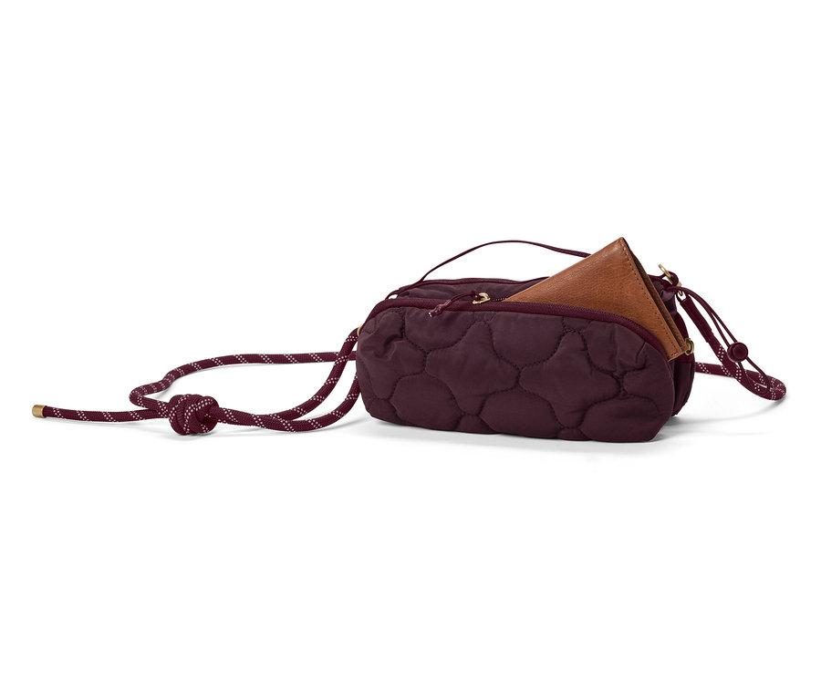 Eine burgunderrote, gesteppte Handtasche mit braunem Portemonnaie darin und einem dicken Kordelband liegt auf einem weißen Hintergrund.