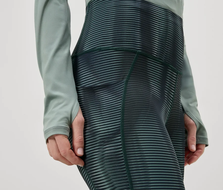 Nahaufnahme einer Person in Leggings mit horizontalem Streifenmuster und einem langärmligen Oberteil in Grün.