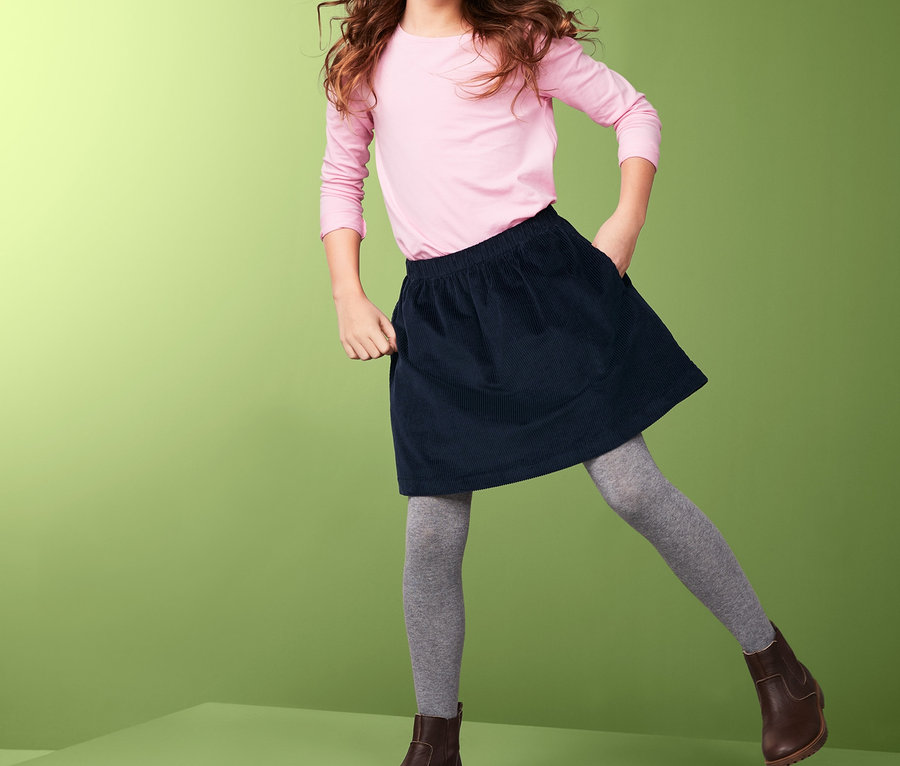 Lächelndes Mädchen posiert in einem rosa Langarmshirt und einem dunkelblauen Cordrock.