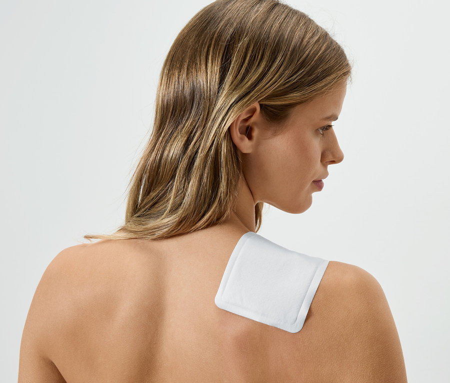 Frau mit einem weißen Wärmepflaster auf der Schulter, Blickrichtung nach rechts.