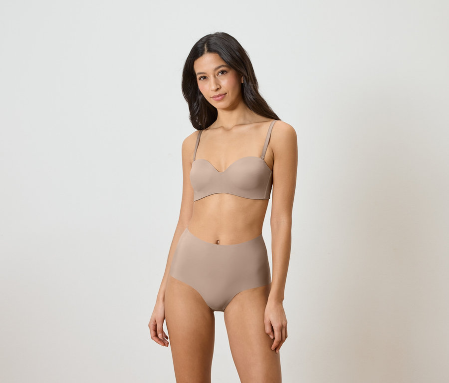Frau trägt einen trägerlosen BH und hochtaillierte Slips in Beige.