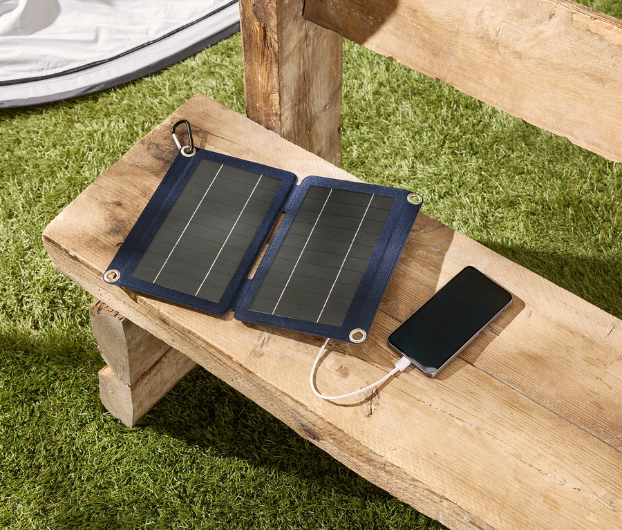 Eine Solarpanel-Ladestation lädt ein Smartphone auf einer Holzbank im Freien.
