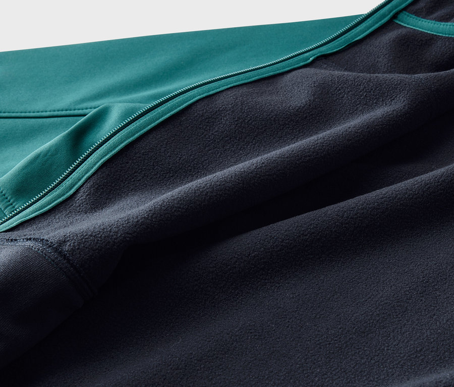 Nahaufnahme einer Jacke mit einer glatten, türkisfarbenen Außenseite und einem dunkelblauen Fleecefutter, getrennt durch einen türkisfarbenen Reißverschluss.