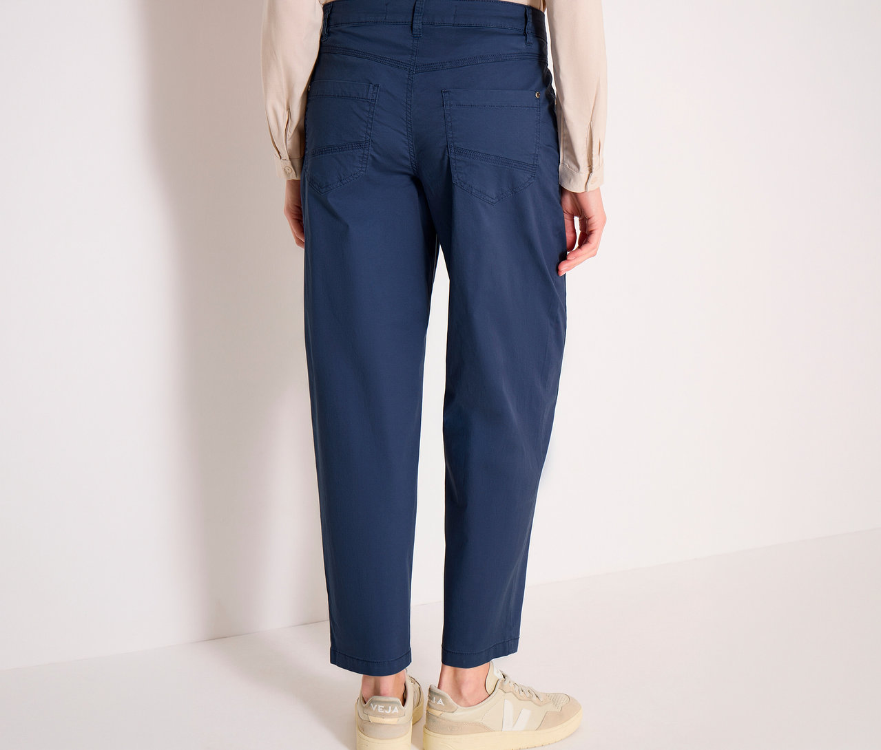 Eine Person von hinten, die blaue CECIL Barrel »Scarlett« Hose, ein helles Hemd und helle Sneaker trägt.