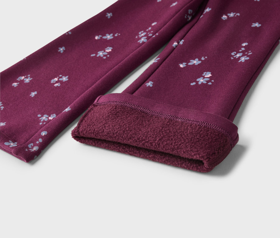 Ein Paar dunkelrote Leggings mit kleinem hellblau-weißem Blumenmuster. Ein Bein ist umgeschlagen, um ein dickes, flauschiges, dunkelrotes Fleecefutter zu zeigen.