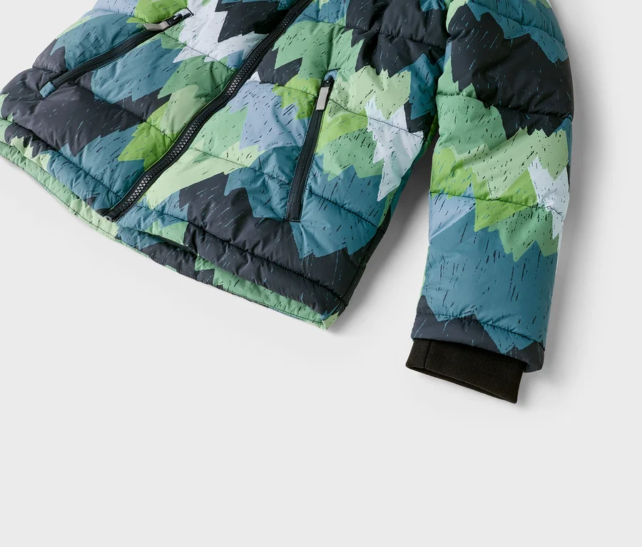 Nahaufnahme einer Steppjacke mit geometrischem Muster aus grünen, blauen, grauen und weißen Zackenformen. Die Jacke hat einen schwarzen Reißverschluss vorne, eine Reißverschlusstasche und ein dunkles Rippbündchen am Ärmel.