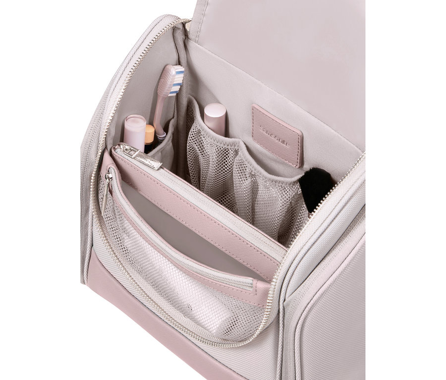 Offene hellgraue und rosa Samsonite Kulturtasche mit verschiedenen Fächern, die eine rosa Zahnbürste, kleine Flaschen und einen Make-up-Pinsel enthält.