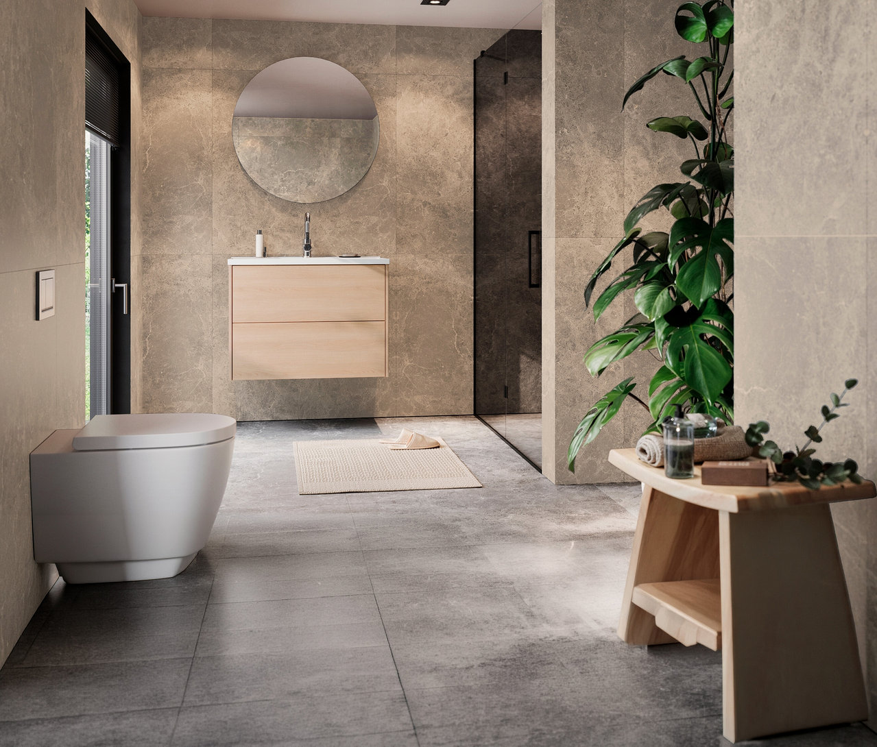 Modernes Badezimmer mit einem 81 cm breiten Waschtisch »Bodera« in Eichenoptik und Becken unter einem runden Spiegel. Links eine wandhängende Toilette, rechts eine Duschkabine und eine große Pflanze. Vorne rechts steht ein Holzhocker mit Handtüchern.