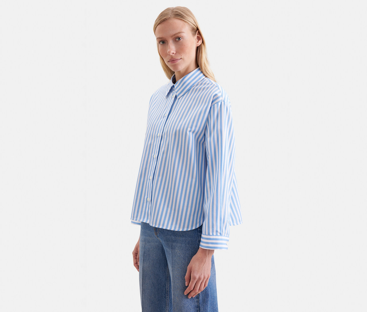 Eine Frau trägt eine blau-weiß gestreifte Seidensticker Oversize Hemdbluse und blaue Jeans.