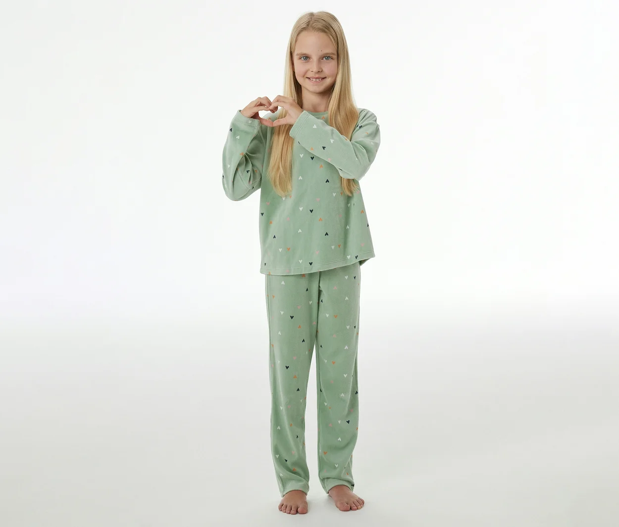 Lächelndes Mädchen mit blonden Haaren im hellgrünen SCHIESSER Kinder-Velours-Pyjama »Herzchen«, das mit den Händen ein Herz formt.