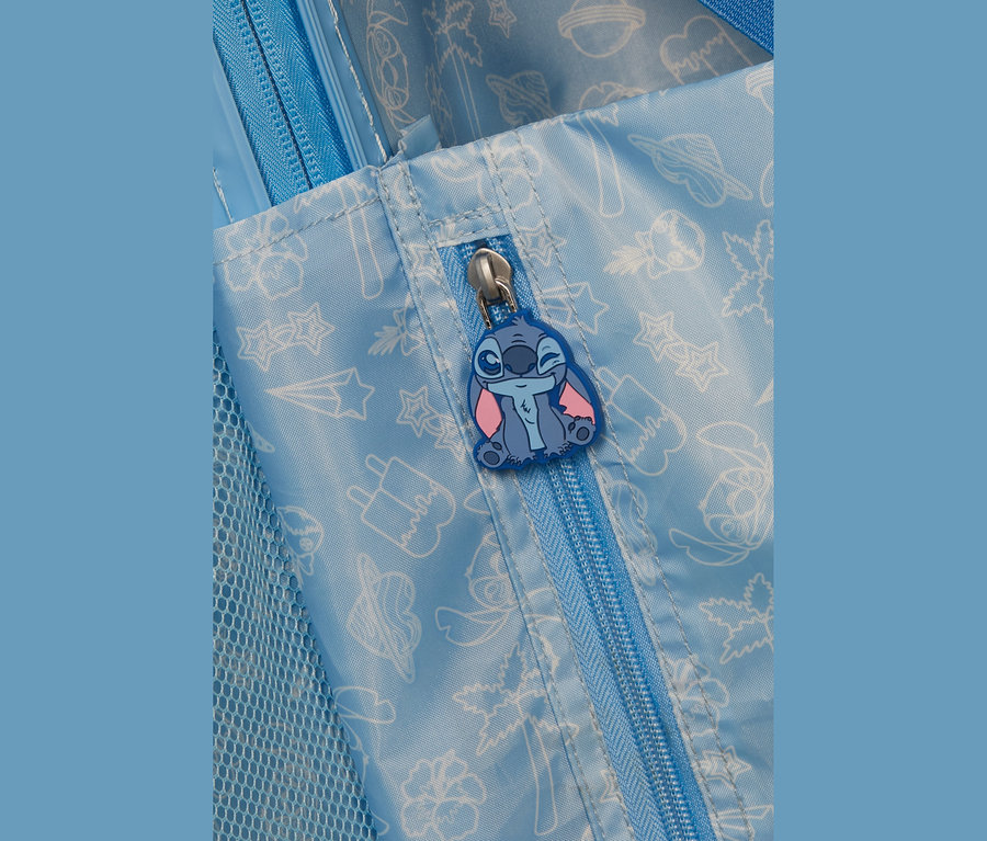 Nahaufnahme eines hellblauen Stoffartikels mit blauem Reißverschluss. Ein zwinkernder blauer und pinker Stitch-Charakter ist am Reißverschlusszipper befestigt. Der Stoff hat weiße Umrisszeichnungen von Sternen und Eis. Links ist blaues Netzgewebe sichtbar.