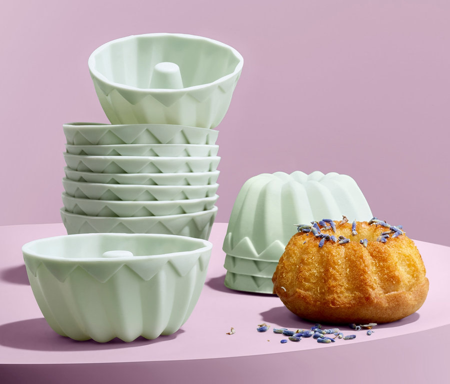 Auf lila Hintergrund stehen 12 Mini-Gugelhupfformen, ein Gugelhupf ist mit Lavendel bestreut.