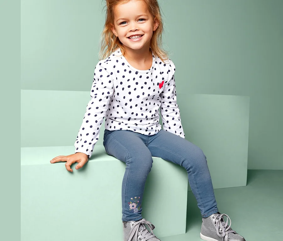 Mädchen sitzt und trägt ein gepunktetes Oberteil und Treggings.