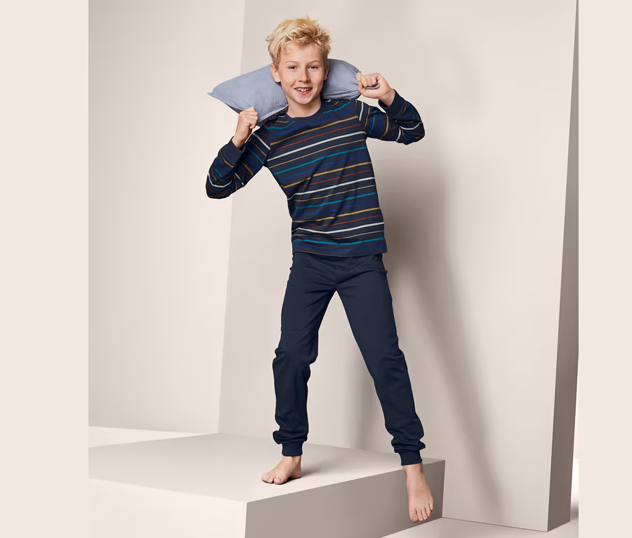 Junge mit Pyjama hält ein Kissen im Nacken und steht auf einer Plattform.