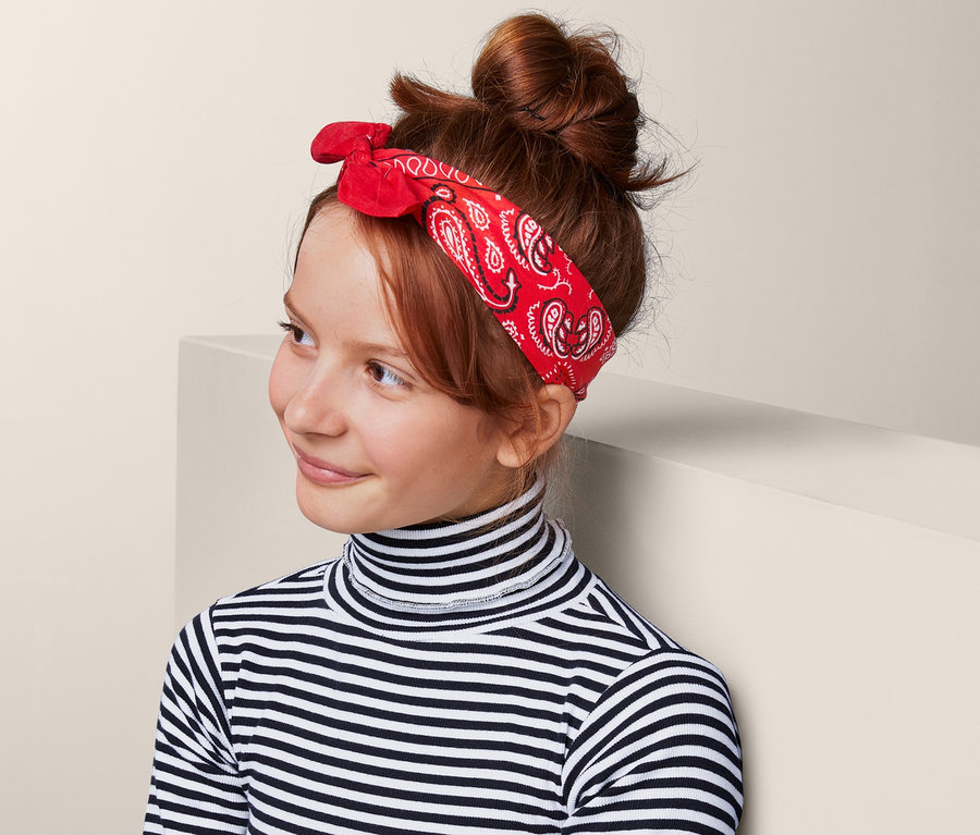 Mädchen mit rotem Bandana-Nickituch im Haar, das ein Paisley-Muster hat. Sie trägt einen gestreiften Rollkragenpullover und einen Jeansrock.