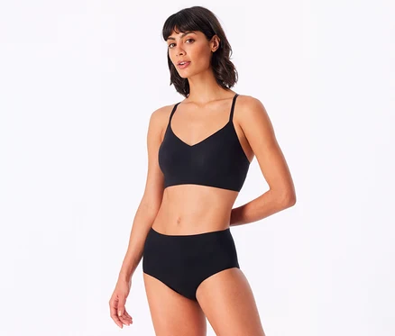 Eine Frau mit dunklen Haaren trägt ein schwarzes SCHIESSER Invisible Bustier mit Pads und einen schwarzen High-Waist-Slip.