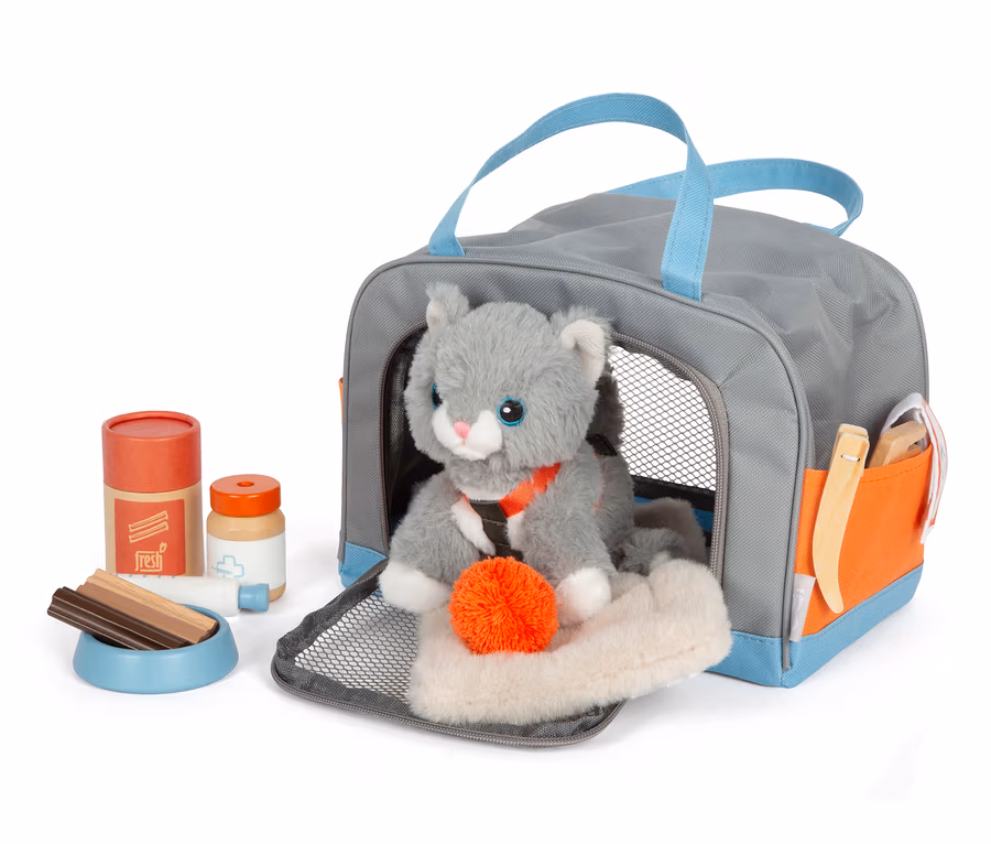 Graue Tasche mit blauen Griffen enthält eine Plüschkatze, daneben eine Schüssel mit Leckerlis und Pflegezubehör. Die small foot Katze mit Tasche und Pflege-Set ist sichtbar.