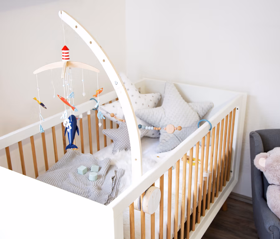 Babybett mit weißem Rahmen, Holzstäben und Sternkissen. Darüber hängt ein small foot Mobile mit Halterung »Seaside« mit maritimen Motiven.