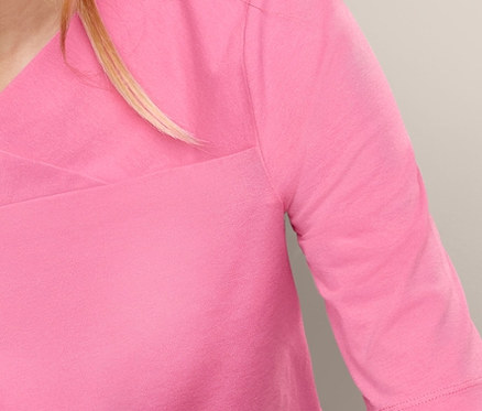 Blonde Frau sitzt und trägt ein rosa Halbarmshirt.