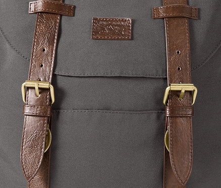 Detailansicht eines grauen Heritage-Rucksacks mit braunen Lederriemen und Messingschnallen.