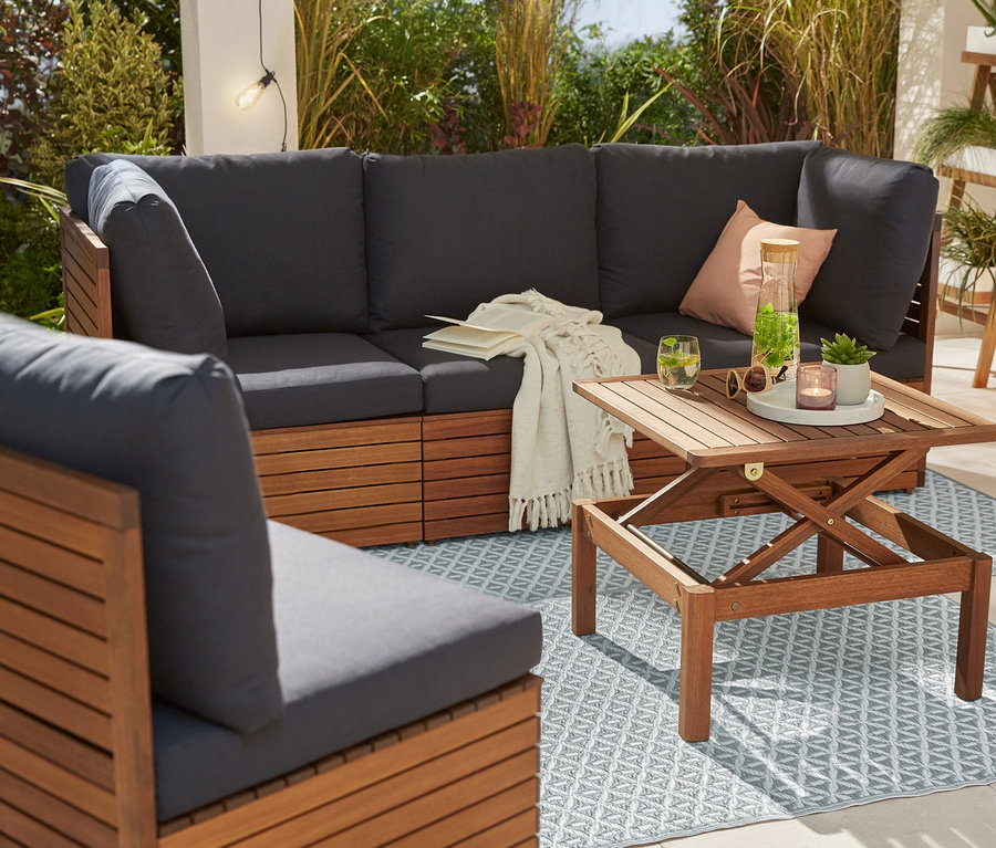 Eine Lounge-Ecke mit Sessel und Outdoortisch auf einem Outdoorteppich. Im Hintergrund eine Pflanzleiter und eine LED-Outdoor-Filament-Laterne.