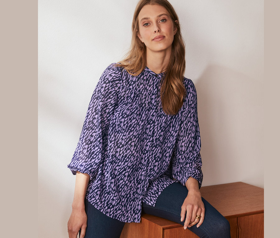 Frau sitzt auf einem Schrank und trägt eine Bluse mit Print.