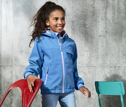 Mädchen trägt eine blaue Softshelljacke mit recyceltem Material und steht.