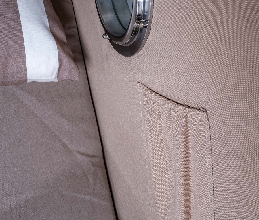 Innenansicht eines Strandkorbs mit gestreiftem Kissen und rundem Fenster.