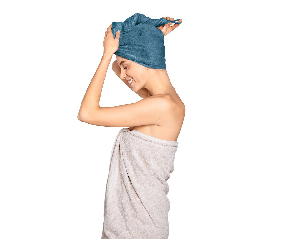 Frau setzt Turban-Handtuch, blau, auf.