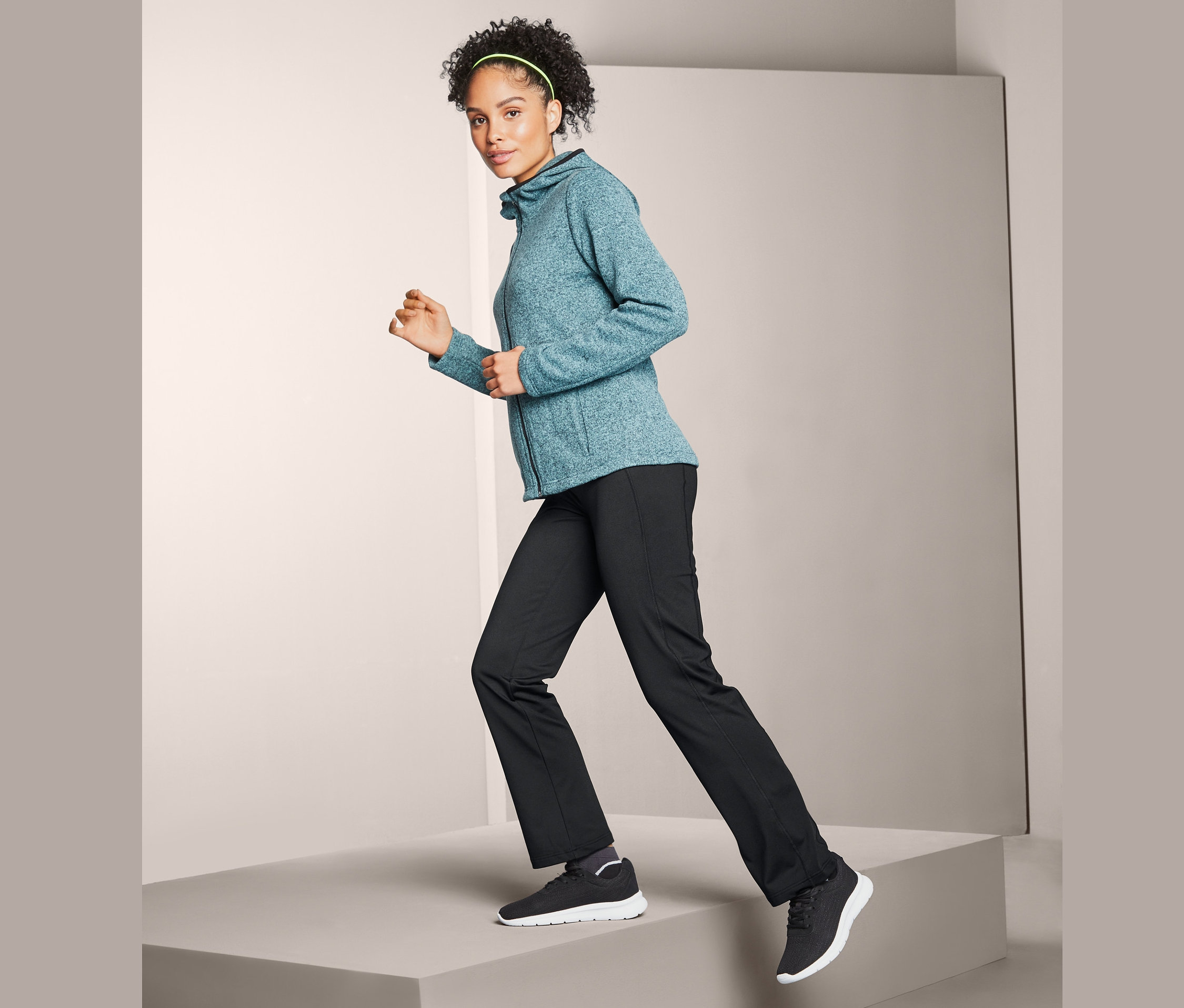 Frau geht auf einem Podest und trägt eine Thermohose, eine Zip-Jacke und Turnschuhe.