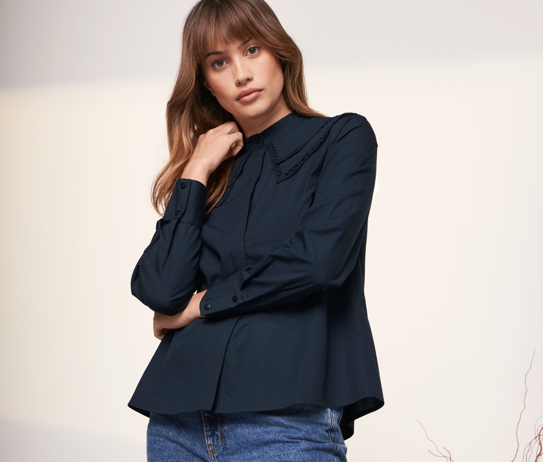 Frau posiert in marineblauer Hemdbluse mit Volantkragen und weiter blauer Jeans.