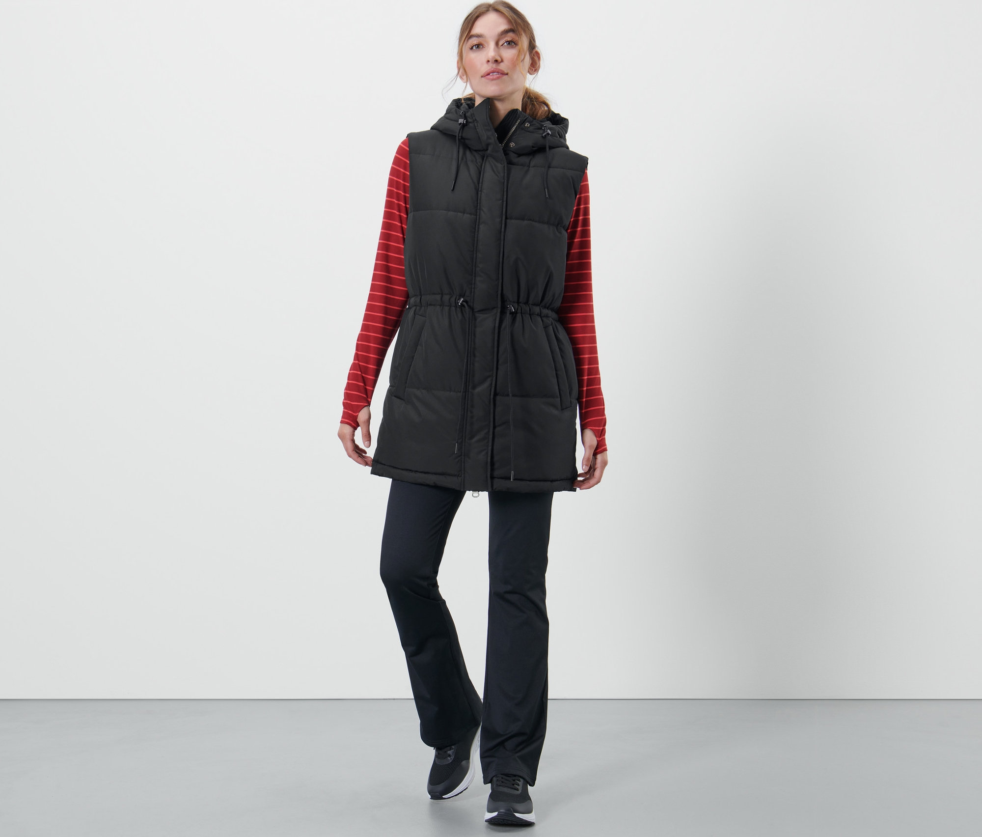 Frau trägt eine Kapuzen-Stepp-Weste, ein rot gestreiftes Langarmshirt und eine schwarze Hose.