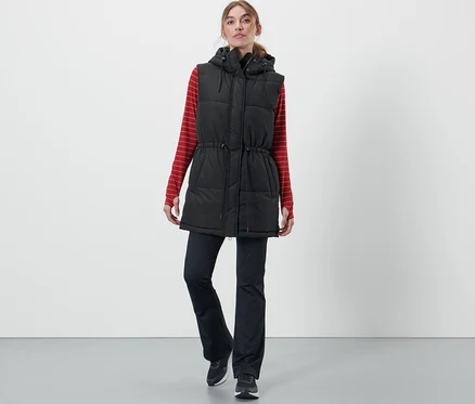 Frau trägt eine Kapuzen-Stepp-Weste, ein rot gestreiftes Langarmshirt und eine schwarze Hose.