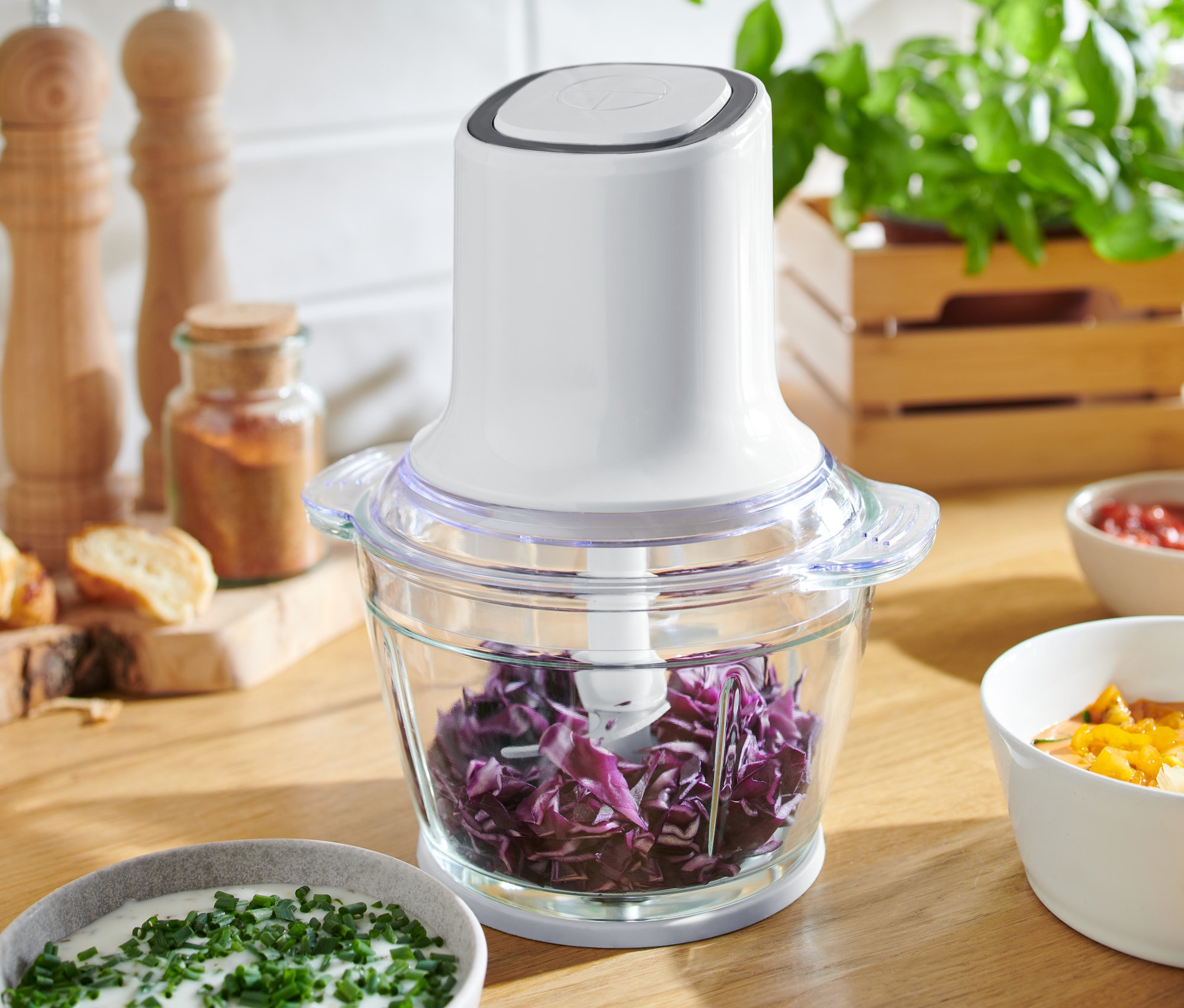 Multizerkleinerer mit geschnittenem Rotkohl auf einem Holztisch mit Schüsseln mit Soße.