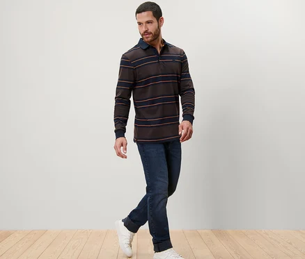 Ein Mann geht und trägt ein Langarm-Poloshirt, Jeans und Turnschuhe.