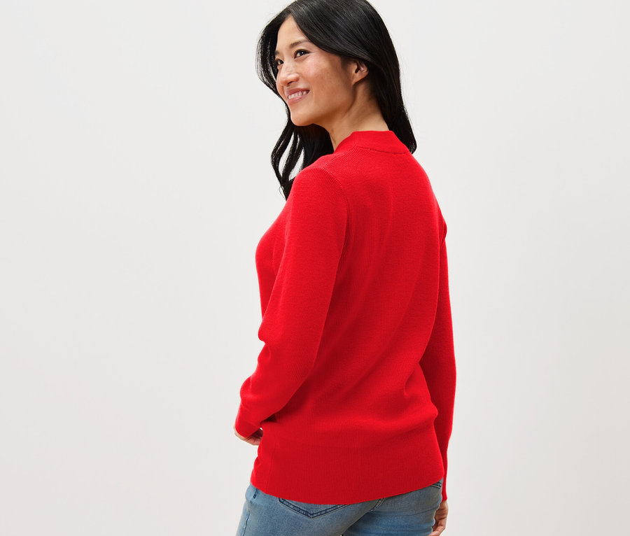 Frau blickt über die Schulter und trägt einen roten Feinstrickpullover und Jeans.