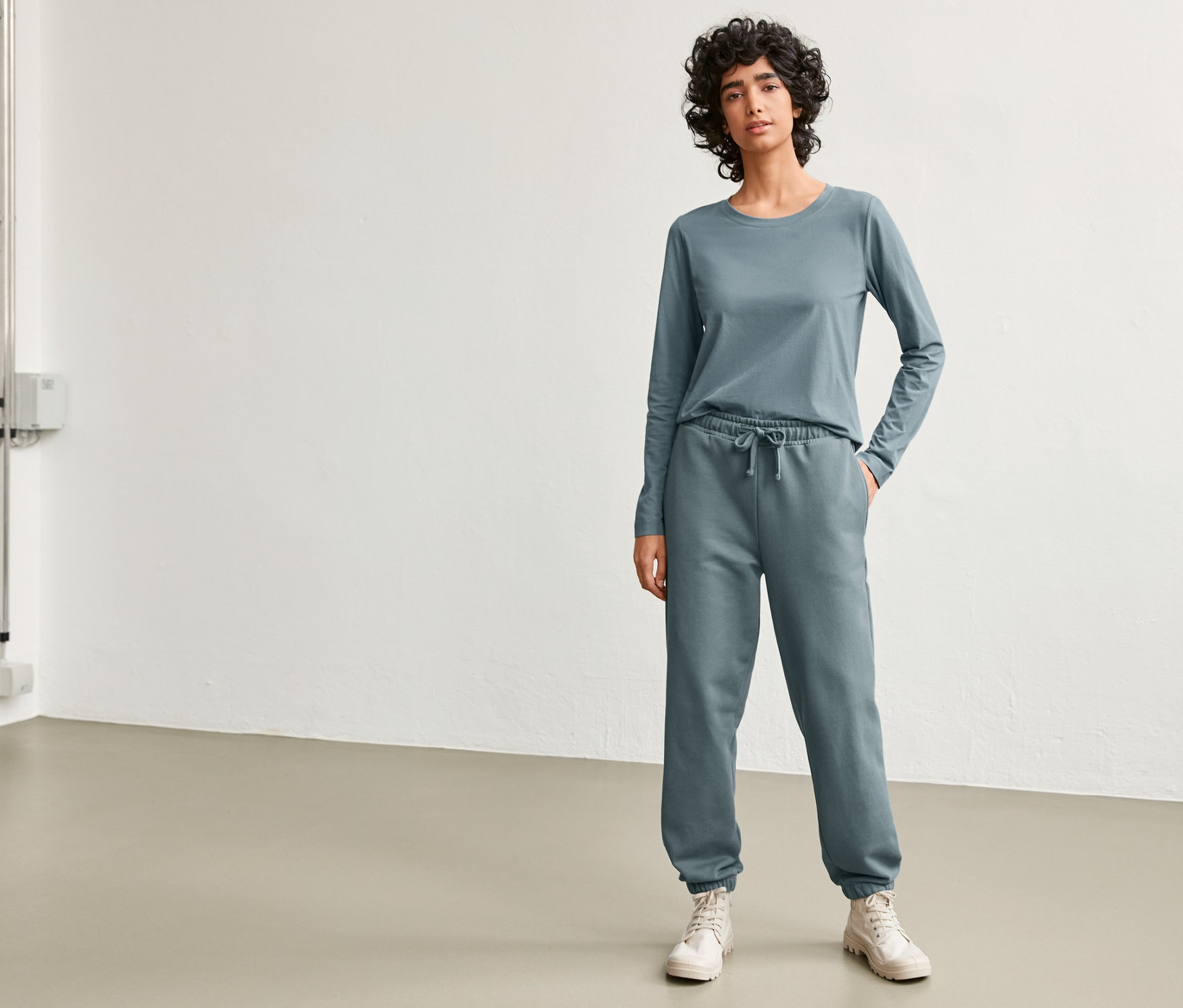 Frau posiert in stone blue NAH/STUDIO Jogginghose und Longsleeve aus nachhaltiger Baumwolle.