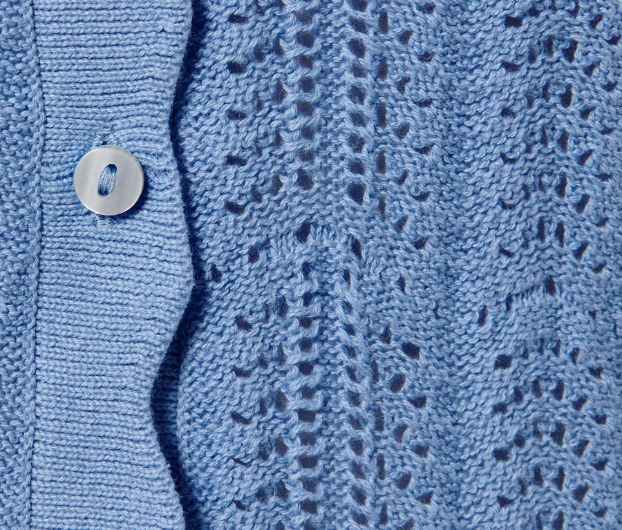 Detailansicht einer blauen Strickjacke mit Ajour-Muster und Knopf.