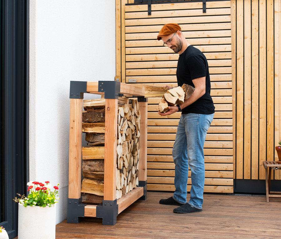 Mann legt Holz in einen Kaminholzständer, L.