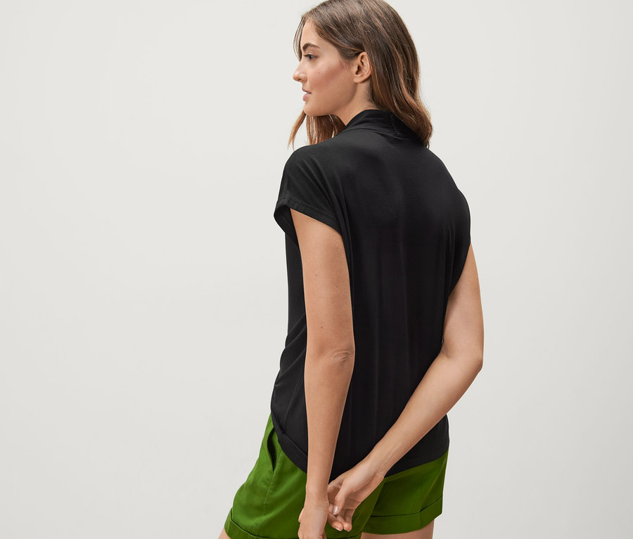 Rückansicht einer Frau, die ein schwarzes Blusenshirt mit V-Ausschnitt und grüne Shorts trägt.