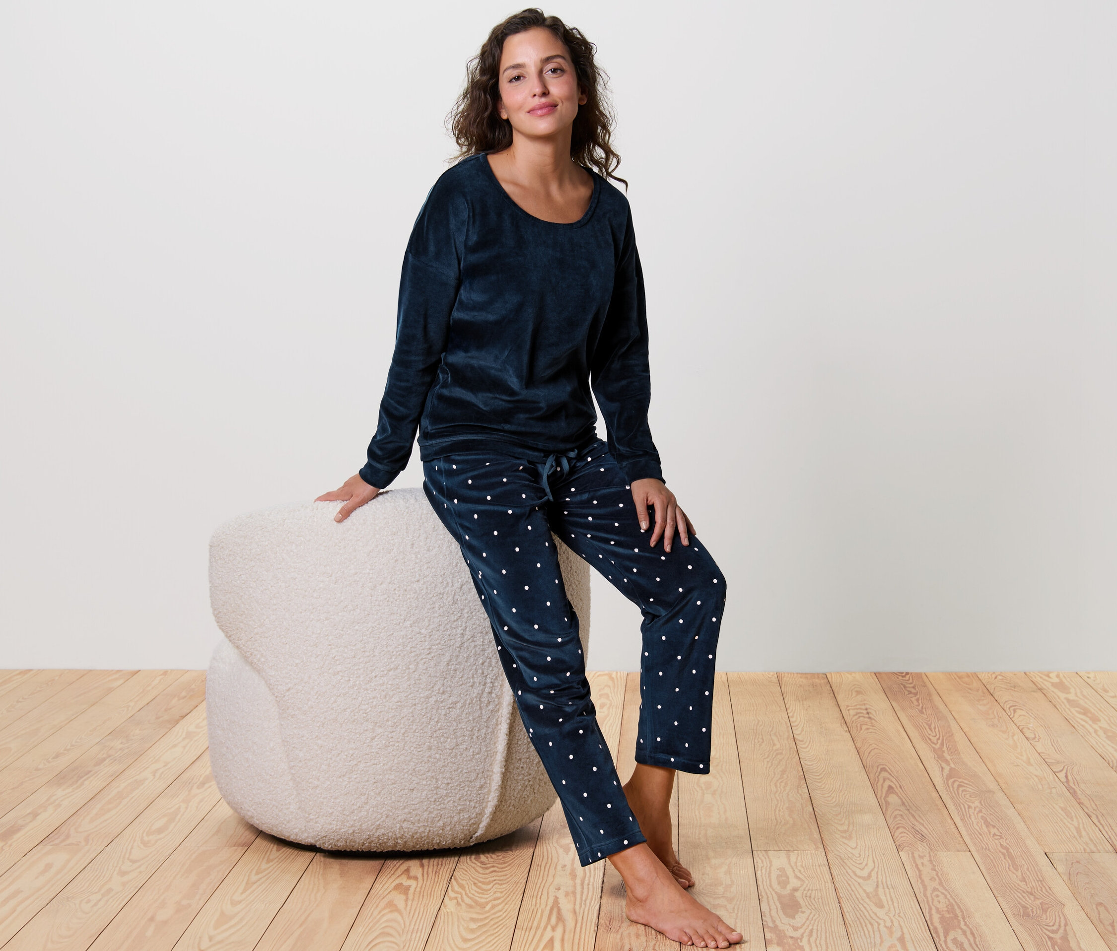 Frau sitzt auf einem weißen Hocker und trägt einen blauen Nicki-Pyjama.