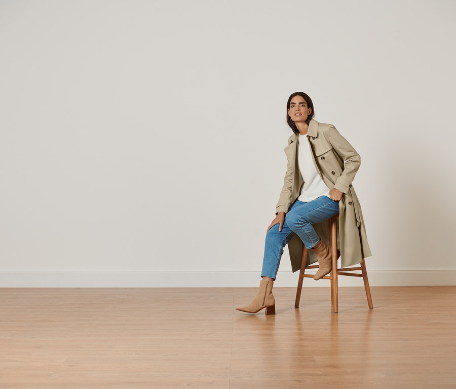 Frau sitzt auf einem Hocker und trägt einen Trenchcoat.