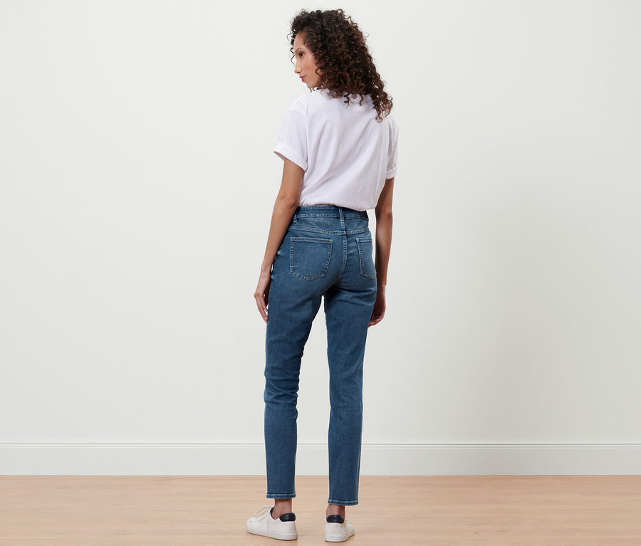 Eine Frau steht mit dem Rücken zur Kamera und trägt eine Slim-Denim »Fit Emma« in Midblue Denim, ein weißes T-Shirt und Turnschuhe.