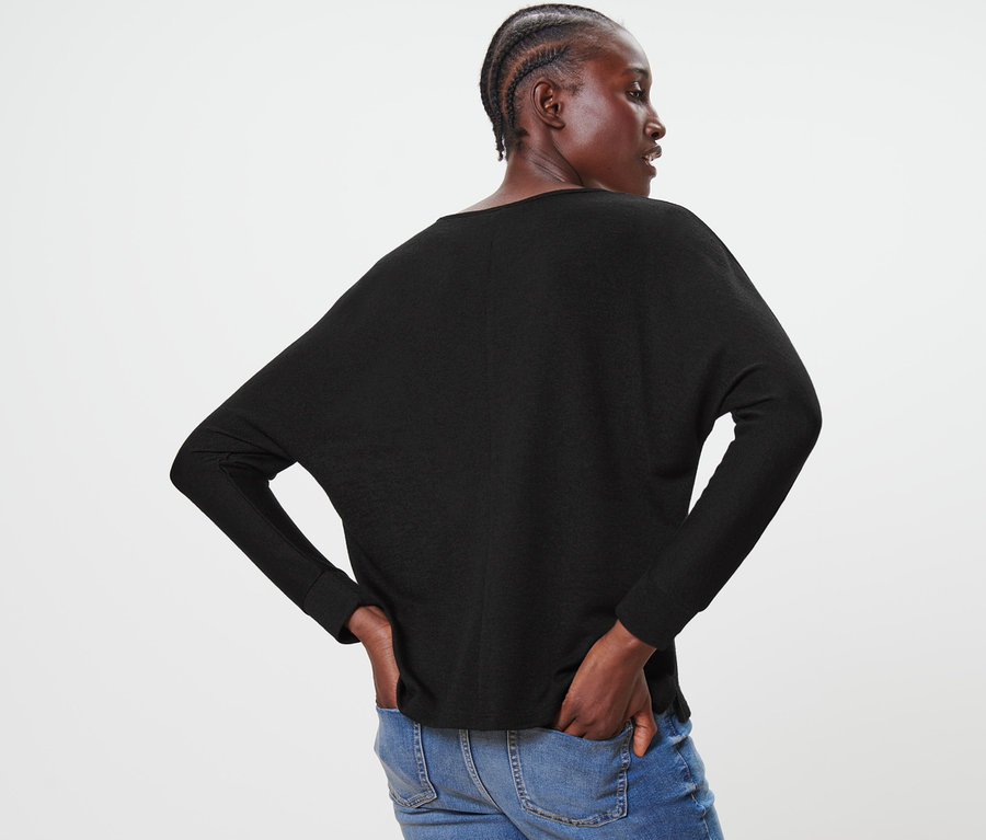 Eine Frau posiert von hinten in einem schwarzen Fledermausshirt und blauen Jeans.